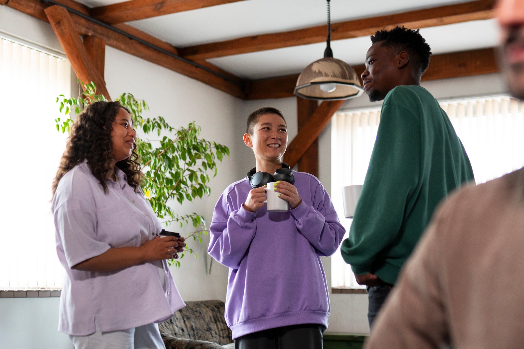 Un grupo de personas conversando de pie, con caf&eacute;, en un espacio luminoso