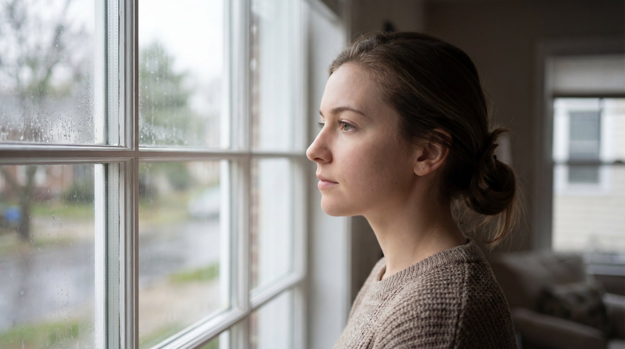 Una mujer mira por la ventana, pensativa, con luz de d&iacute;a