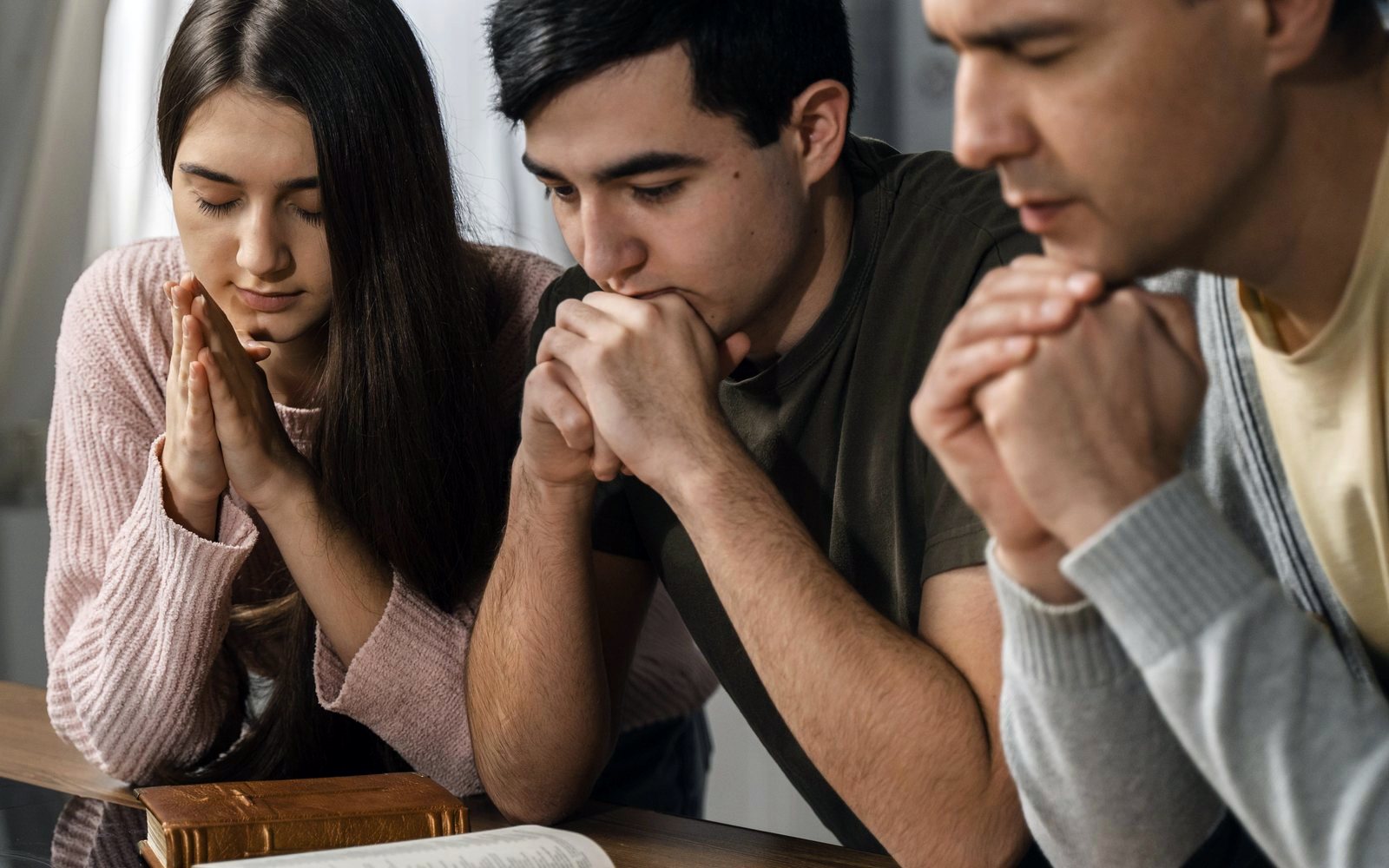 Tres personas orando juntas con la Biblia abierta sobre la mesa